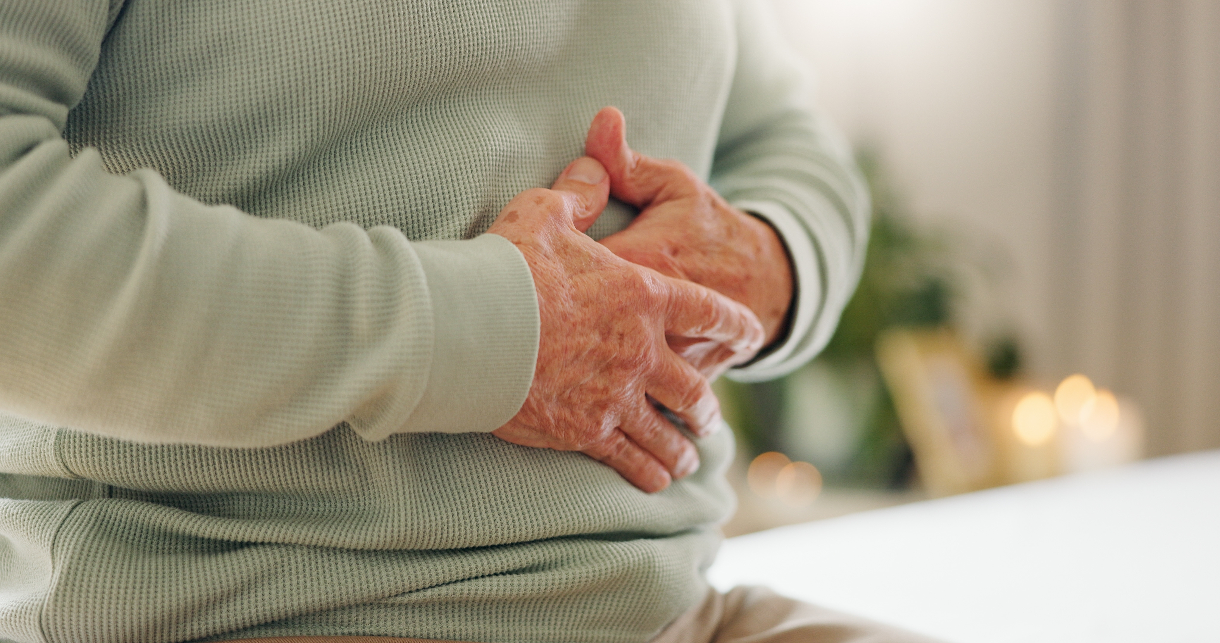 Older person holding their stomach because it hurts wearing a green sweater